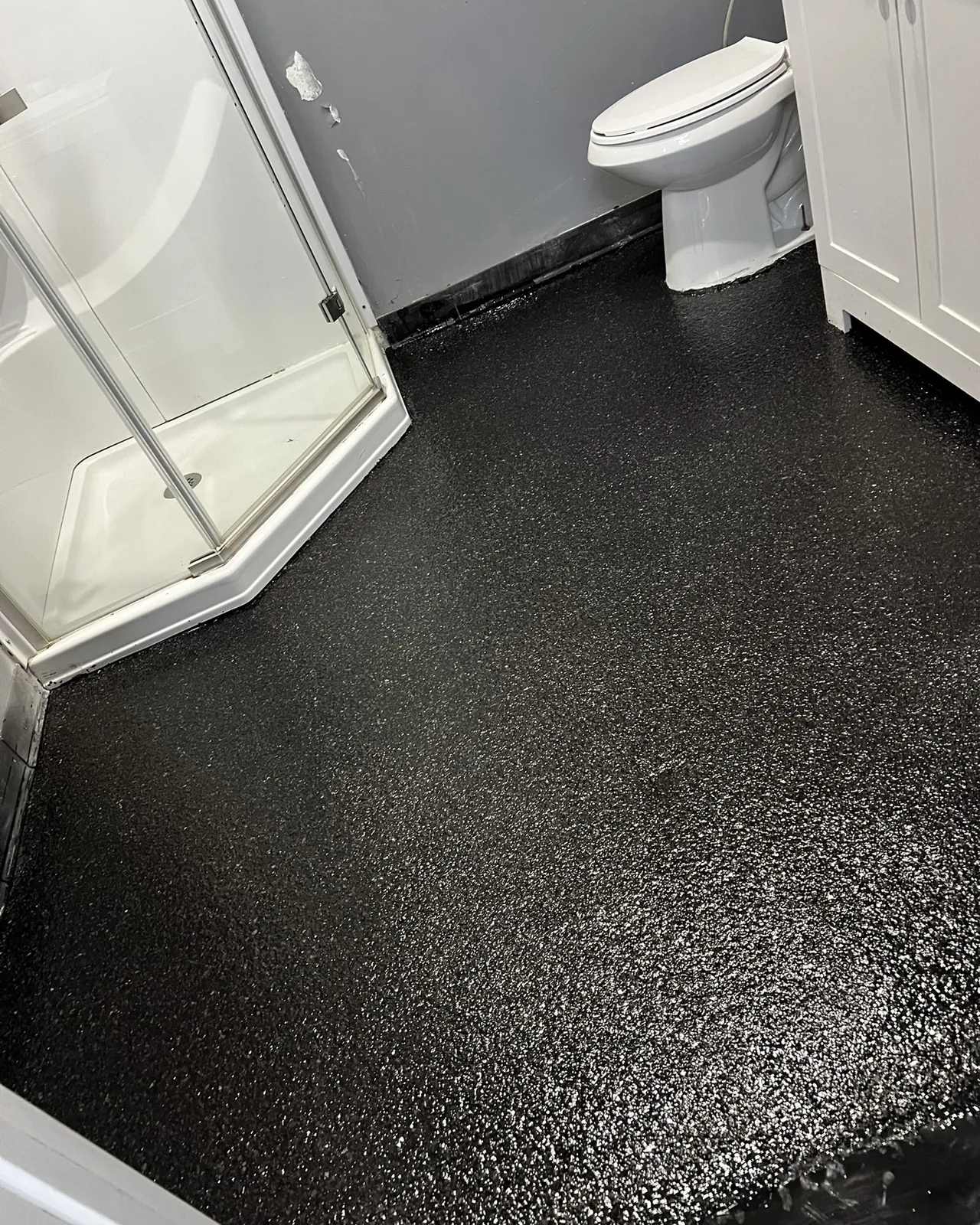 Bathroom floor in black flake, coved up to the wall around the shower and vanity