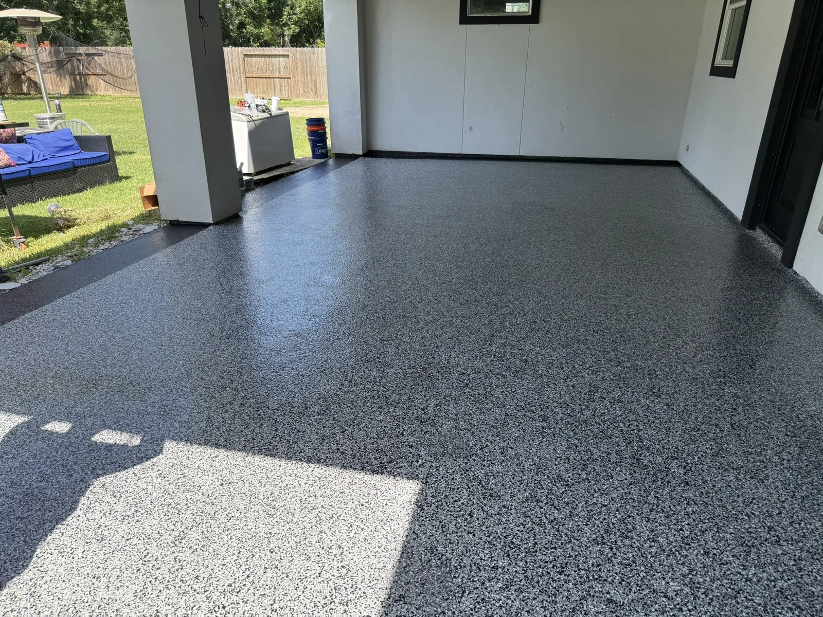 Covered patio in grey flake, back yard and fence past the posts