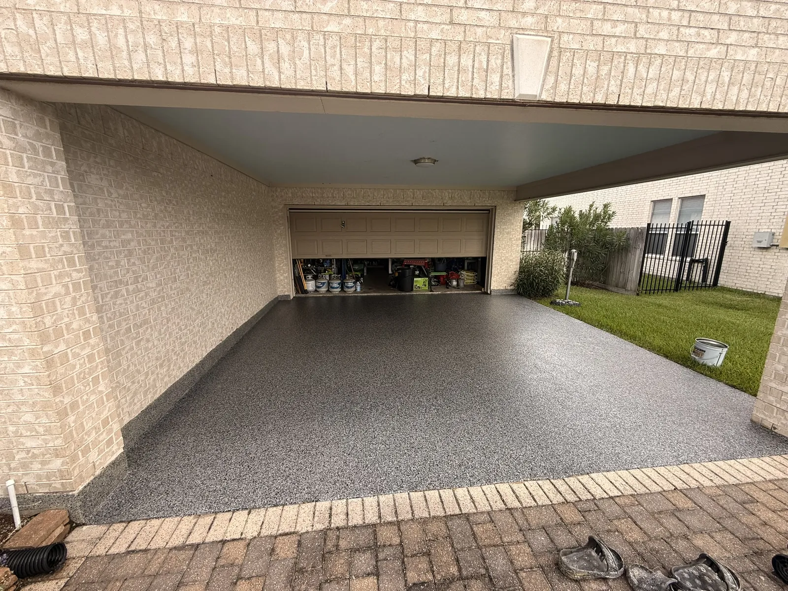 Covered drive-through porch coated in grey flake with brick paving in front of it